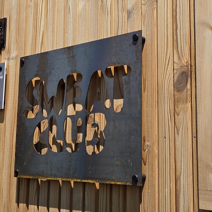 SweatClub&rsquo;s name cut out of a steel plate, bolted to the sauna&rsquo;s larch cladding.